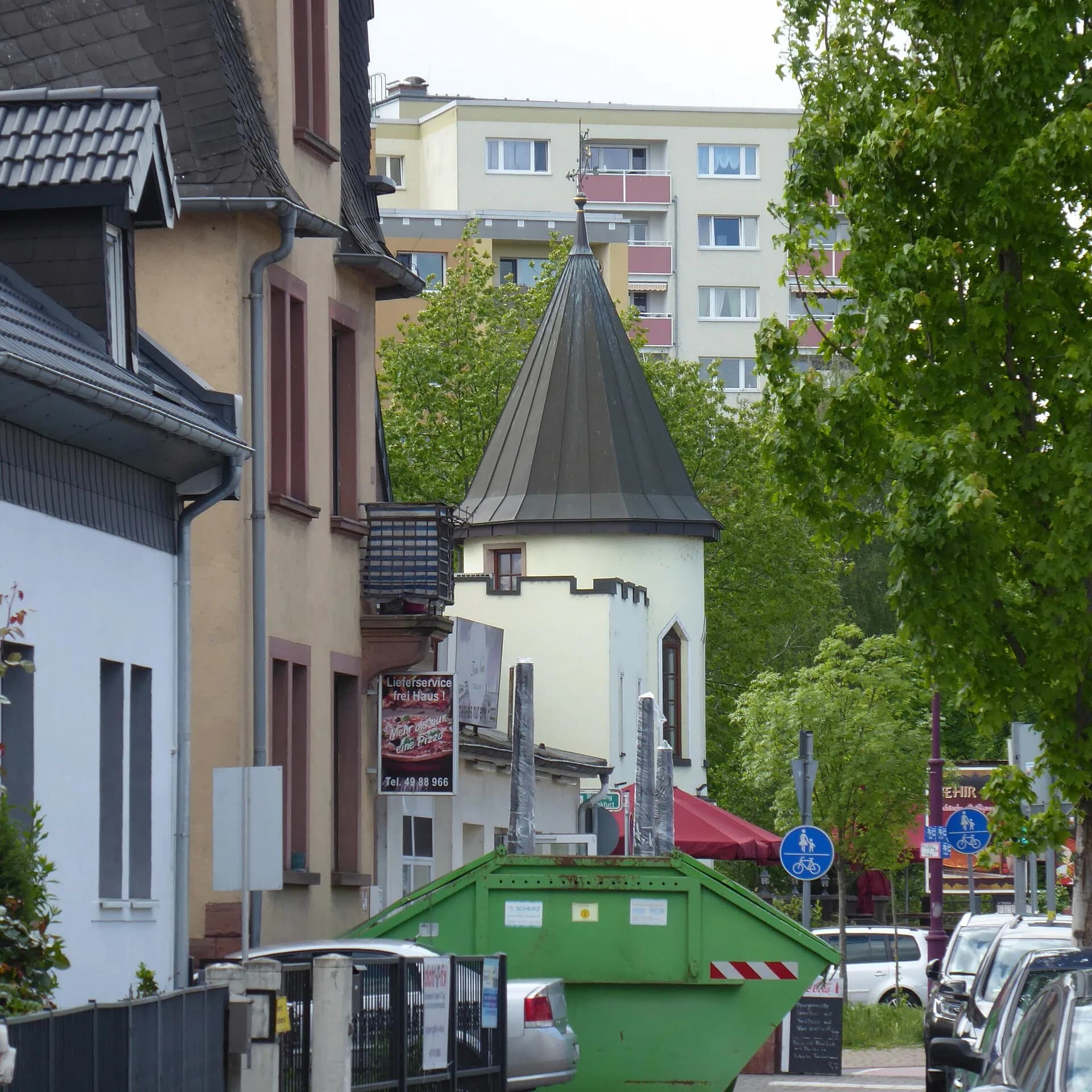 Blick entlang der Kennedystraße auf einen spitzbehelmten Turm in Maintal-Dörnigheim