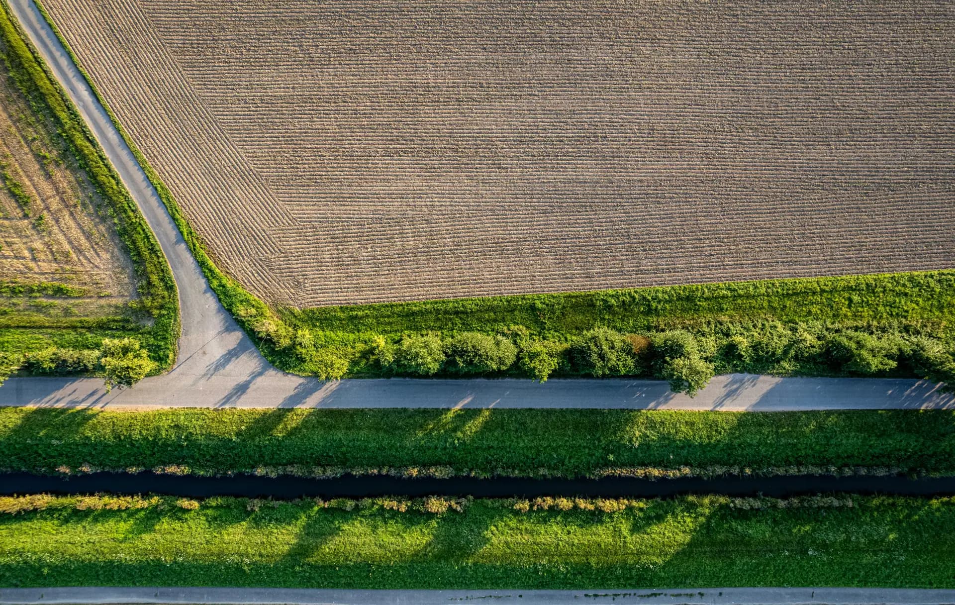 Luftbild eines gepflügten Ackers mit Feldweg, Hecken und Wassergraben