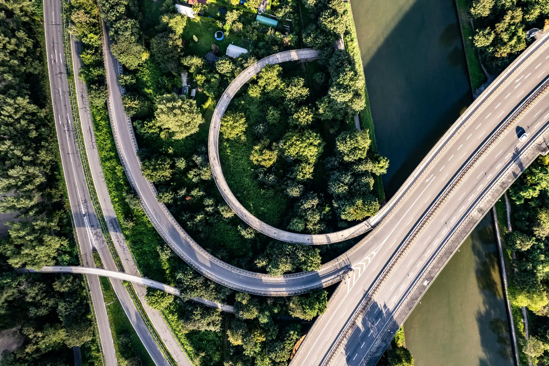 Luftbild einer Straßenschleife zwischen Bäumen, Kanal und Kleingärten
