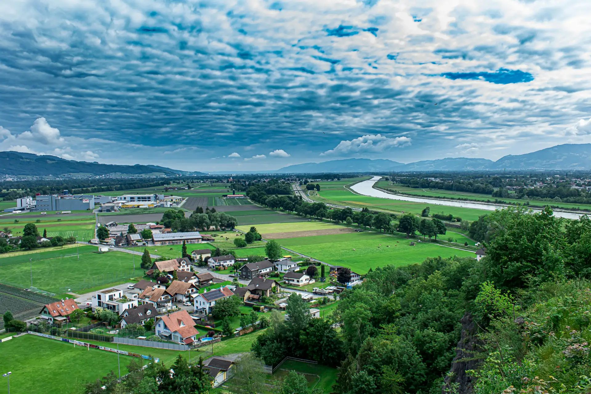 Blick über ein Flusstal mit Dorf, Feldern und Sportplätzen