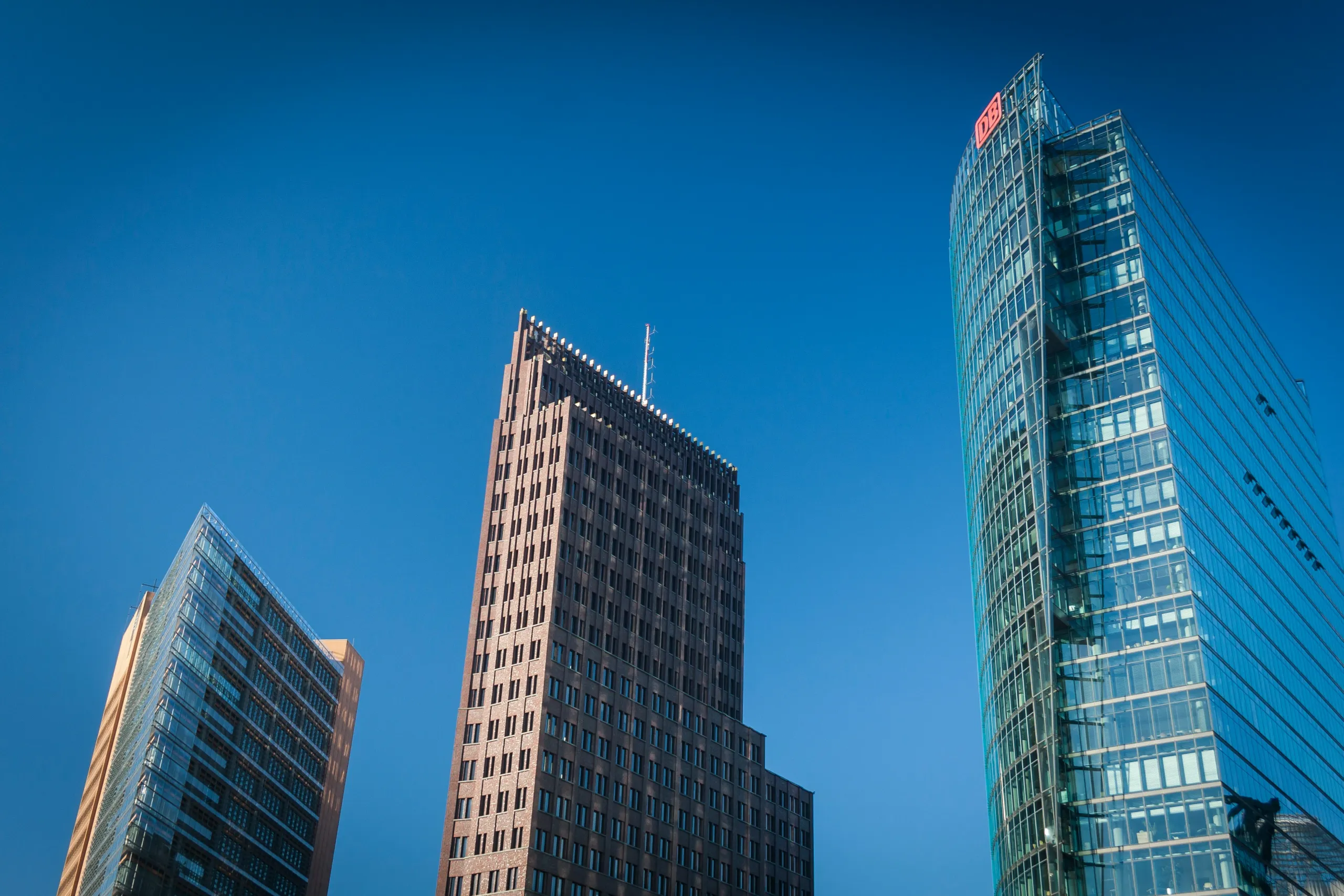 Drei Bürotürme mit Glas- und Steinfassaden vor blauem Himmel